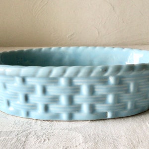 May include: A light blue ceramic bowl with a woven basket design. The bowl is oval shaped and has a smooth, glazed finish.