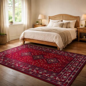 Könnte beinhalten: Ein roter rechteckiger Teppich mit einem aufwendigen floralen und geometrischen Muster. Der Teppich hat einen tiefroten Hintergrund mit einem dunkleren Rand und zentralen Medaillons. Der Teppich liegt in einem Schlafzimmer mit Holzbett.