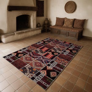 May include: A large, rectangular patchwork rug with a geometric pattern in shades of red, black, orange, and cream. The rug is placed on a tiled floor in a room with a fireplace and bench seating.