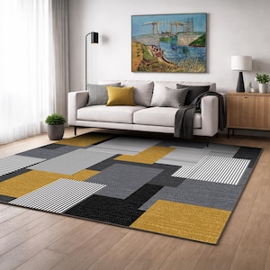 Könnte beinhalten: Moderner Teppich mit geometrischem Muster aus schwarzen, grauen, weiß gestreiften und senfgelben Rechtecken. Der Teppich liegt auf einem Holzboden in einem Wohnzimmer.