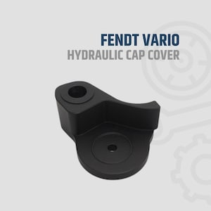 May include: A black hydraulic cap cover with the text "FENDT VARIO HYDRAULIC CAP COVER" in white and blue. The cap cover has a curved design with a circular opening and a flat base. The product is made of metal.