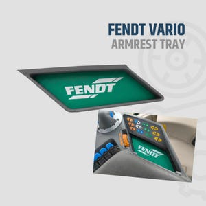 Può includere: Un vassoio bracciolo Fendt Vario grigio con un inserto verde con il logo Fendt bianco. L'immagine mostra anche un pannello di controllo del trattore con il logo Fendt.