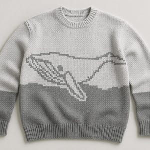 Peut inclure: Un pull gris clair à col rond et manches longues. Le pull présente un motif de baleine pixélisée en gris plus foncé sur la poitrine. Le bas du pull est gris plus foncé.