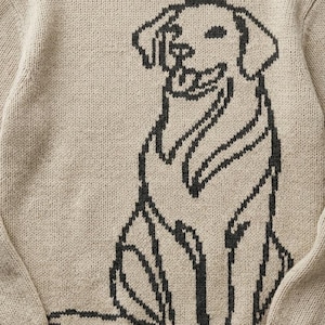 May include: Beige knit sweater featuring a black outline of a dog. The dog is sitting with its tongue out. The sweater has a crew neck and long sleeves. A cozy and casual apparel item.