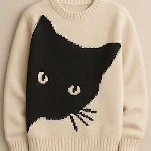 May include: Cream-coloured jumper with a large black cat face design. The cat's silhouette is on the front, with eye and whisker details. Ribbed cuffs and hem complete the look. A cosy knitwear item.
