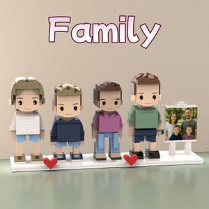 Puede incluir: Una exhibición con temática familiar con cuatro figuras de bloques con varios atuendos y peinados. Un pequeño marco de fotos muestra un retrato familiar. La palabra "Family" está escrita encima de las figuras. Dos corazones rojos se colocan frente a las figuras.