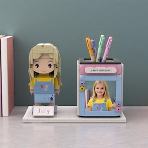 Puede incluir: Un organizador de escritorio estilo Lego con una figura rubia y un portalápices con el texto "HAPPY BIRTHDAY". El portalápices tiene una foto de una niña. La figura tiene la palabra "July" en un pequeño letrero.