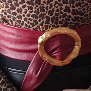 May include: A wide red leather belt with a large gold-toned buckle. The belt is wrapped around a person wearing a leopard print top.