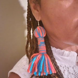 May include: A pair of long, colorful tassel earrings. The earrings are made of yarn in shades of blue and orange. The tassels are long and flowing, and the earrings are a statement piece.