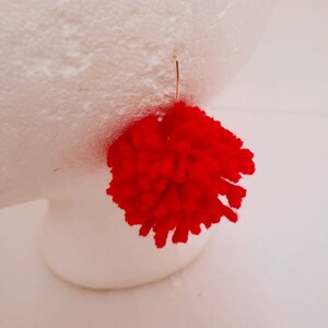 May include: Red pom-pom earrings with a gold hook.