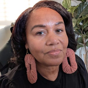 May include: A woman wearing a black shirt with large, pink, crocheted hoop earrings.