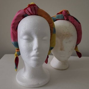 May include: Two colorful fabric headbands with a knotted design. The headbands are made of a soft, stretchy fabric and are perfect for adding a pop of color to any outfit.
