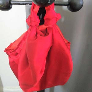 May include: A bright red fabric bag with a knotted handle. The bag is made of a soft, silky material and is folded into a compact shape.