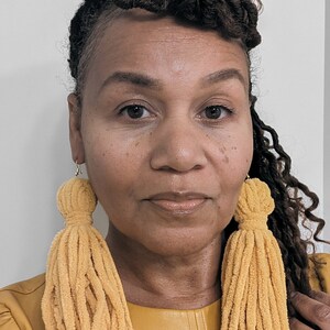 May include: A person wearing a mustard yellow leather jacket with long, mustard yellow tassel earrings.