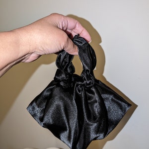 May include: A black satin handbag with knotted handles. The bag is small and compact, perfect for carrying essentials.