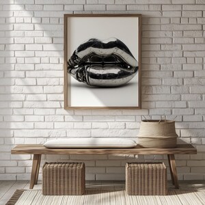 Può includere: Una stampa incorniciata con una scultura metallica cromata di labbra. L'opera d'arte è esposta su uno sfondo bianco, contro un muro di mattoni bianchi. Una panca in legno con cesti intrecciati e un cesto intrecciato sono in primo piano.