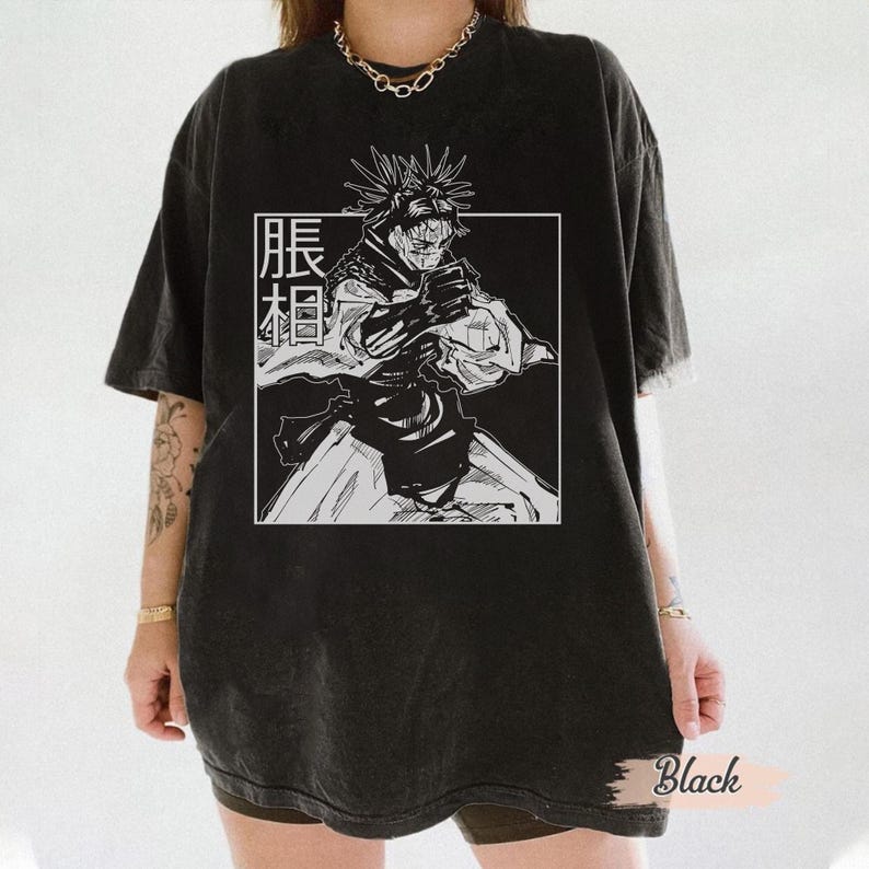 May include: Black t-shirt featuring a black and white graphic of a character from an anime series. The graphic is inside a white rectangle with Japanese text. The shirt has short sleeves and a relaxed fit.