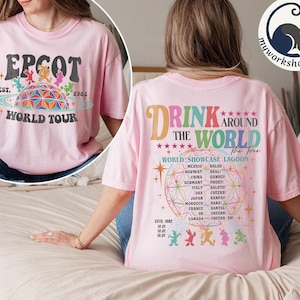Könnte beinhalten: Hellrosa T-Shirt mit "EPCOT World Tour" Grafik auf der Vorderseite, mit farbenfrohem geometrischem Design und Text. Auf der Rückseite des Shirts steht "Drink Around The World" mit einer Liste von Ländern und Phrasen. Bequemer, lässiger Stil.