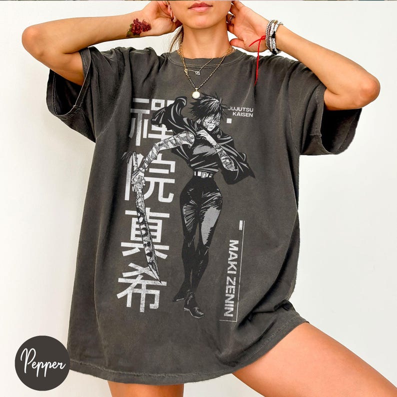 May include: Dark grey oversized t-shirt featuring a graphic of a female anime character with Japanese text. The character is holding a weapon. The text "JUJUTSU KAISEN" and "MAKI ZENIN" are also printed on the shirt.