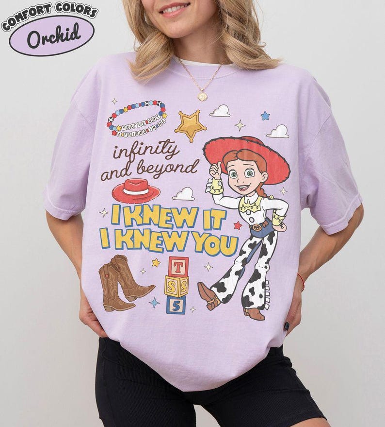 May include: A light purple t-shirt featuring a graphic print of a cowgirl character, a red hat, brown cowboy boots, a gold star, alphabet blocks, and a beaded bracelet. The text reads infinity and beyond, I KNEW IT, I KNEW YOU, and You've got a friend in me.
