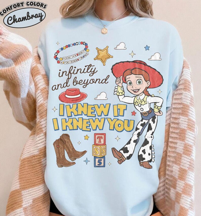 May include: A light blue crewneck sweatshirt featuring a graphic print of Jessie from Toy Story, a red cowboy hat, brown boots, a beaded bracelet, and alphabet blocks. The text reads infinity and beyond, I KNEW IT, I KNEW YOU, and YOU'VE GOT A FRIEND IN ME.
