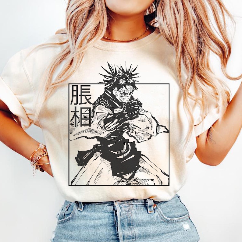 May include: Cream-colored t-shirt featuring a black and white anime-style illustration of a character within a rectangular frame. The character has spiky hair and is in a dynamic pose. Japanese text is vertically aligned on the left side of the frame.