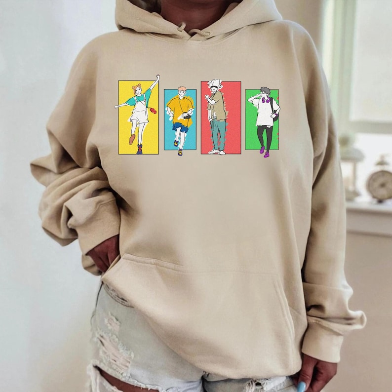 May include: Beige hoodie featuring a colorful graphic of four anime-style characters in rectangular frames. The characters are in various poses and outfits, with a yellow, blue, red, and green background.