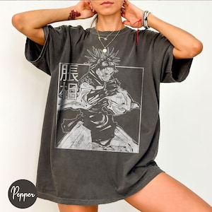 May include: Dark gray oversized t-shirt featuring a black and white graphic of an anime character within a rectangular frame. The shirt has Japanese text on the left side of the graphic. The shirt has short sleeves and a relaxed fit.