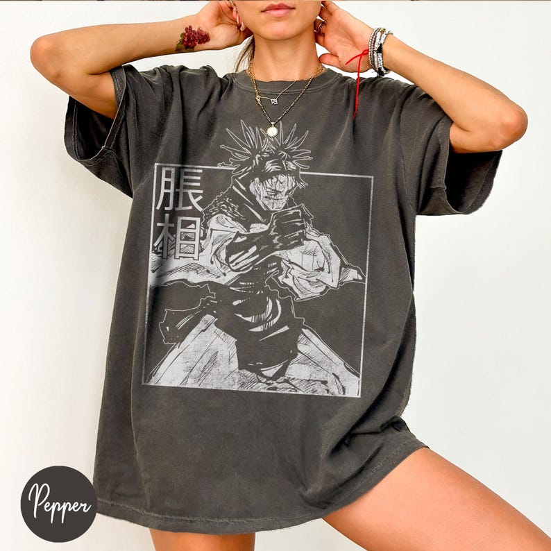 May include: Dark gray oversized t-shirt featuring a black and white graphic of an anime character within a rectangular frame. The shirt has Japanese text on the left side of the graphic. The shirt has short sleeves and a relaxed fit.