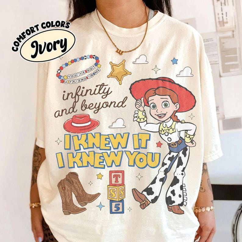 May include: An ivory t-shirt featuring a graphic print of the character Jessie from Toy Story, a red cowboy hat, brown cowboy boots, a beaded bracelet, and alphabet blocks. The text reads "infinity and beyond" and "I KNEW IT I KNEW YOU".