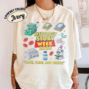May include: Ivory-colored t-shirt with a graphic design featuring histology-related illustrations and text. The design includes a microscope, lab equipment, and the words "HISTOLOGY STORY WEEK 2026" and "SLICE, SLIDE, AND DECIDE."