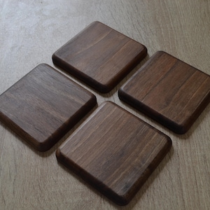May include: Four square wooden coasters with rounded edges, arranged in a diamond shape. The coasters are a rich, dark brown color, showcasing the natural wood grain. They appear to be handmade and are suitable for protecting surfaces from drink rings.