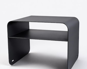 May include: A matte black metal side table featuring a continuous curved frame that forms both the top and the sides, with a single horizontal shelf positioned in the middle. The structure has a smooth, solid surface and a small rectangular cutout.