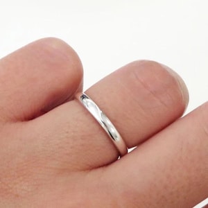 May include: A simple, polished silver-colored band ring with a smooth, rounded surface. The metal has a reflective, high-shine finish that catches the light, creating a clean and uniform appearance around the entire circumference of the circular ring.