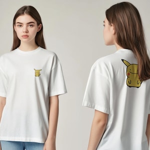 K&ouml;nnte beinhalten: Wei&szlig;es T-Shirt mit einer kleinen gelben Pikachu-Grafik auf der Vorderseite und einem gr&ouml;&szlig;eren Pikachu-Design auf der R&uuml;ckseite. Das T-Shirt hat einen Rundhalsausschnitt und kurze &Auml;rmel. Das Design ist im Cartoon-Stil.