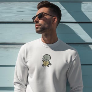 K&ouml;nnte beinhalten: Wei&szlig;es Sweatshirt mit einem Cartoon-Schildkr&ouml;ten-Design auf der Vorderseite. Die Schildkr&ouml;te hat einen grauen Kopf, einen gelben Panzer und ein l&auml;chelndes Gesicht. Das Sweatshirt ist einfarbig wei&szlig;.