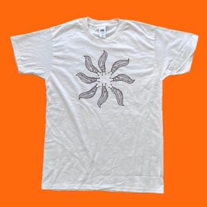 Pode incluir: Uma t-shirt branca de manga curta com uma estampa gráfica circular de oito lesmas castanho-escuras dispostas num padrão radial. A peça tem gola redonda e uma etiqueta de marca visível na parte interna da gola, centrada no peito.