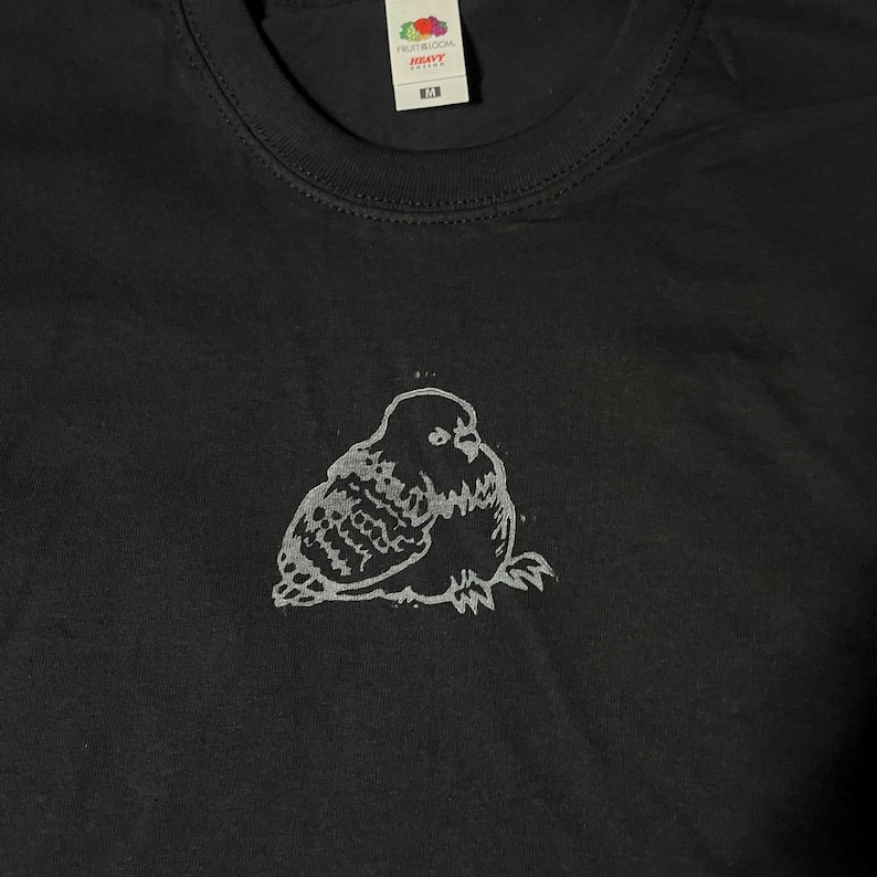 May include: Black t-shirt with a white graphic of a stylized owl. The shirt has a crew neck and short sleeves. The brand logo is visible at the top of the shirt.