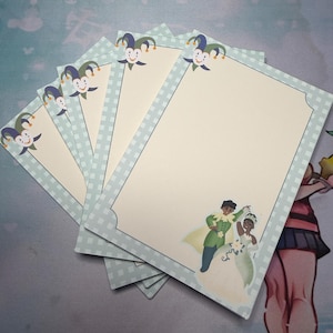 May include: A stack of stationery cards with a light blue checkered border and a cartoon jester at the top. The cards feature an illustration of a couple dancing. The background is a light blue and white pattern.