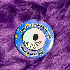 May include: A round button with a blue background and the text "Explain to daddy Bubble How bad thing". The button features a smiling face with a gradient of colors and a set of sharp teeth. Yellow stars are around the edge.
