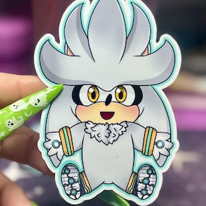 Puede incluir: Una pegatina con un personaje de dibujos animados con pelaje plateado y ojos grandes y amarillos. El personaje tiene una cabeza blanca con pelo puntiagudo, un contorno azul claro y está sentado. La pegatina tiene un contorno azul claro.