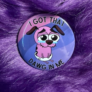 May include: A round button featuring a cartoon dog with large, expressive eyes and tears, set against a pink, blue, and purple background. The text "I GOT THAT DAWG IN ME" is printed on the button.