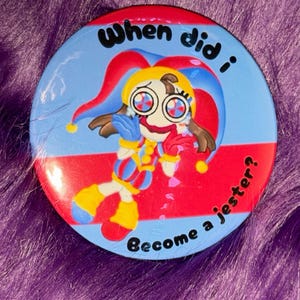 May include: A round button with a cartoon jester design. The button features a blue background with the text "When did I become a jester?" The jester has a yellow hat, red and blue outfit, and large eyes.