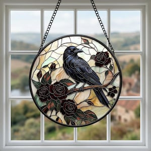 Puede incluir: Vidriera redonda que representa un cuervo negro posado en una rama con rosas rojas oscuras. La obra de arte está enmarcada en negro y colgada de una cadena. El fondo muestra una vista del paisaje a través de una ventana.