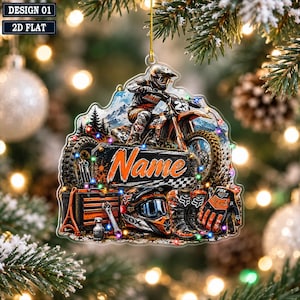 May include: A flat, decorative ornament featuring a motocross rider on a dirt bike, a toolbox, a helmet, boots, and gloves. The design includes the word Name in orange script on a rectangular sign, set against a mountain backdrop with colourful lights.