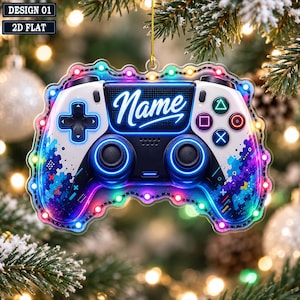 May include: A flat, decorative ornament shaped like a video game controller, featuring a white and black color scheme with blue and purple paint splatter accents. The center displays the word Name in white script, surrounded by colorful LED lights.