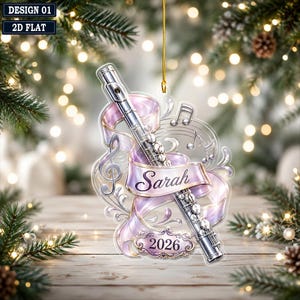 May include: A clear, flat, hanging ornament featuring a silver flute wrapped in a light purple ribbon. The ribbon displays the name Sarah in cursive script. A decorative plaque at the bottom reads 2026, accompanied by musical notes and a treble clef.