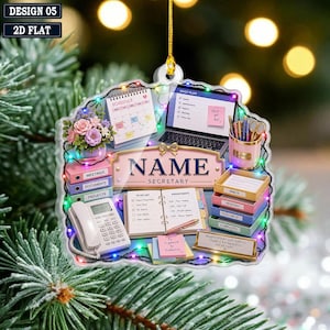 May include: A flat, decorative ornament featuring a desk scene with a calendar, laptop, telephone, stacked file trays, and a nameplate labeled NAME SECRETARY. The design is outlined with colorful string lights and includes a gold hanging cord.