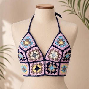 May include: A halter-style crop top constructed from multiple crocheted granny squares. The squares feature a repeating pattern of light blue, yellow, white, and dark brown centers, all bordered by dark navy blue yarn and light pink yarn.