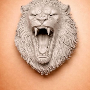 May include: A detailed, gray lion head sculpture with an open mouth, showcasing sharp teeth and a long tongue. The lion's mane is textured, and the sculpture is set against a peach-colored background. This artwork is a decorative wall hanging.